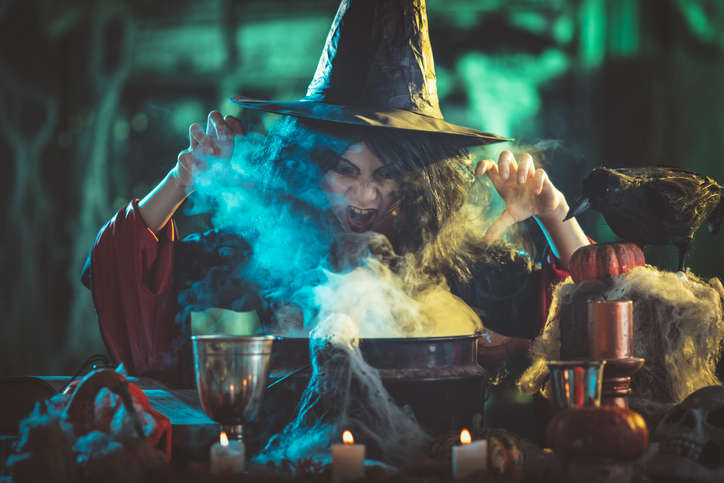 Close-up of young witch with awfully face in creepy surroundings full of steam and fog, tells evil words to magic potion.